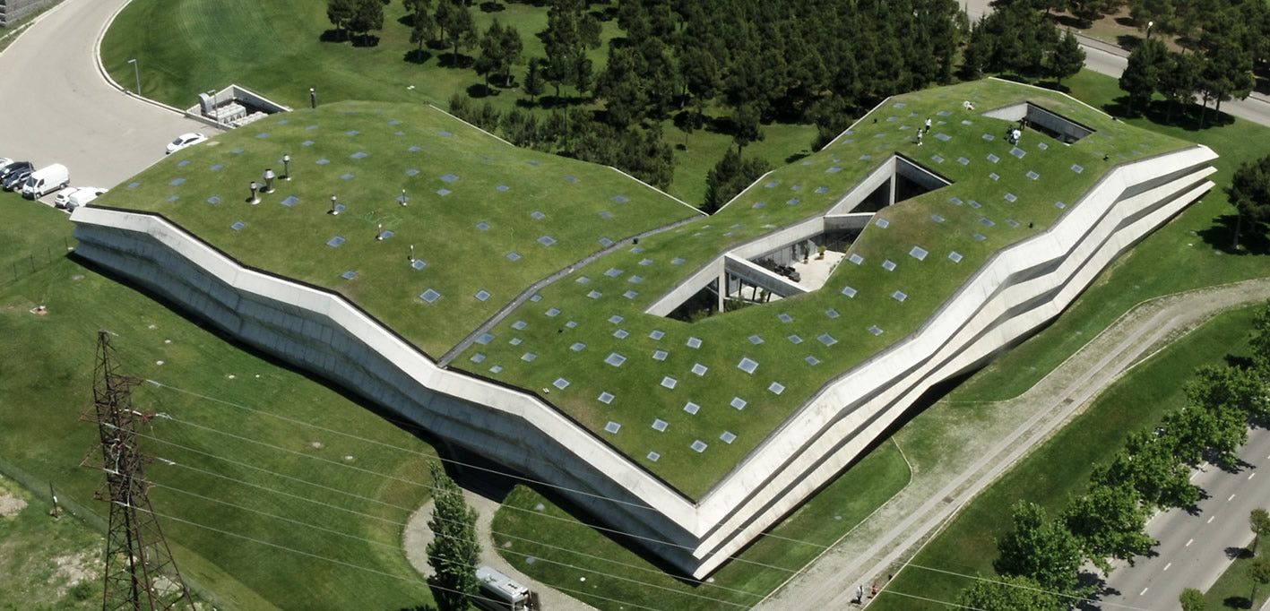 Eine Drohnenaufnahme der Fabrikhalle in Georgien zeigt ein riesiges modernes Gebäude mit grünem Dach, rundherum stehen Bäume, das Gebäude fügt sich harmonisch in die Natur ein