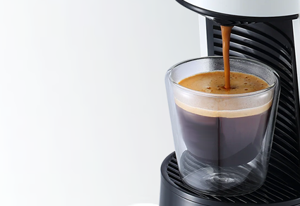 Nahaufnahme der weißen Espressomaschine die einen Espresso in einem doppelwandigem Glas zubereitet
