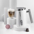 Der weiße Meama Milchschäumer steht auf einem weißen Zylinder, daneben auf einem höheren weißen Zylinder ein Cappuccino in einem Doppelwandigem Glas mit perfektem Milchschaum und Meama Logo