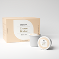 Zwei Multi-Tee-Kapseln der Sorte Creme Brulee stehen im Vordergrund, dahinter die passende Verpackung