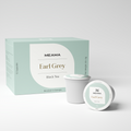 Zwei Multi-Tee-Kapseln der Sorte Earl Grey Schwarztee stehen im Vordergrund, dahinter die passende Verpackung